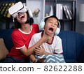 Little boy has fun wearing vr goggles while girl is playing mobile phone. 82622288