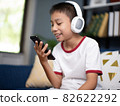 Asian boy wearing headphones and holding a phone. 82622292