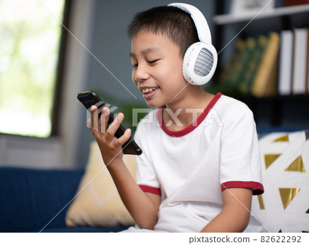 Asian boy wearing headphones and holding a phone. 82622292