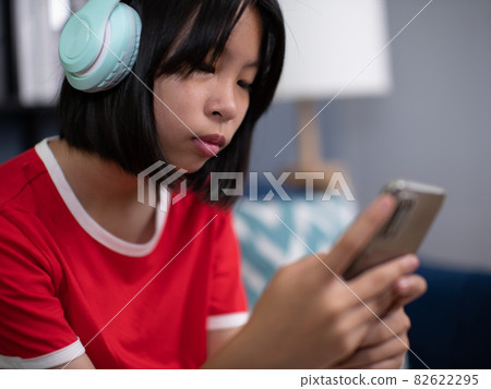 girl wearing headphones using smartphone, interested child listening to favorite music, chatting in social network or playing game online. girl wearing headphones using smartphone, interested child listening to favorite music, chatting in social network or playing game online. 82622295