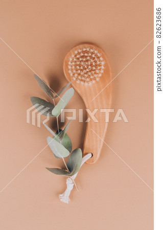 Natural boar bristles exfoliating dry face or body brush with eucalyptus leaves on light brown background. Dry face brush with stiff vegetable fibers. Detoxing skin ritual. Vertical image, mockup Natural boar bristles exfoliating dry face or body brush with eucalyptus leaves on light brown background. Dry face brush with stiff vegetable fibers. Detoxing skin ritual. Vertical image, mockup 82623686