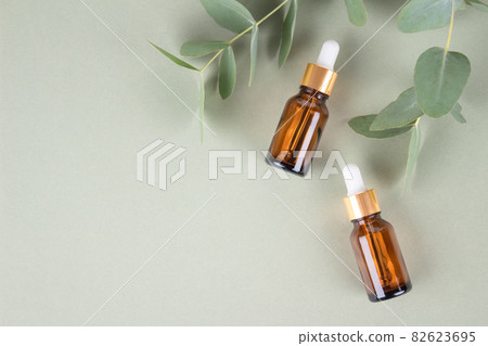 Mockup image of glass dropper bottles with eucalyptus oil. Modern organic cosmetics, facial anti-aging oil. Trendy still life composition with eucalyptus leaves on green background with copy space Mockup image of glass dropper bottles with eucalyptus oil. Modern organic cosmetics, facial anti-aging oil. Trendy still life composition with eucalyptus leaves on green background with copy space 82623695