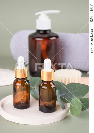 Set of natural beauty treatments - glass dropper bottles with natural organic cosmetics, natural face or body dry brush, eucalyptus oil, cream, lotion, essential oils on green background. Mockup Set of natural beauty treatments - glass dropper bottles with natural organic cosmetics, natural face or body dry brush, eucalyptus oil, cream, lotion, essential oils on green background. Mockup 82623697