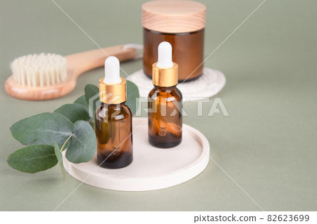 Glass dropper bottles and jars with natural organic cosmetics, natural bristles face or body dry brush - eucalyptus oil, face or body cream, essential oils on green background with copy space. Mockup 82623699