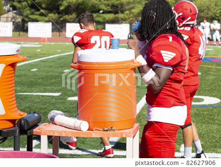 Football player sipping water next to an orange cooler on the sidelines during a game 82627906