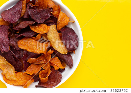 Purple and yellow sweet potato chips in white plate on yellow background. 82628762