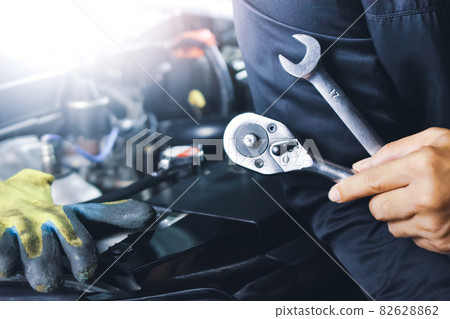 Car mechanic holding combination spanner and socket wrench 82628862