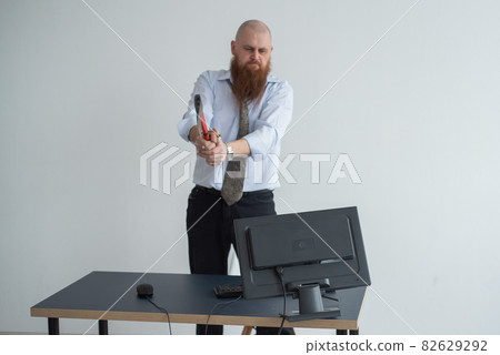 Stressed crazy businessman smashing his computer in office using ax problem concept. The man has problems at work and frustration. 82629292