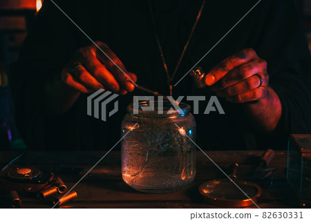 hands of sorcerer alchemist prepare a magic potion poison with herbs in flask at table 82630331