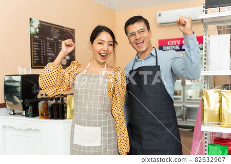 Cheerful business owners standing welcomingly together in front of the counter of their cafe. Cheerful business owners standing welcomingly together in front of the counter of their cafe. 82632907