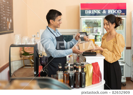 Small business, takeaway food. Happy female customer with bakery taking paper box from man or barman in coffee shop. Small business, takeaway food. Happy female customer with bakery taking paper box from man or barman in coffee shop. 82632909