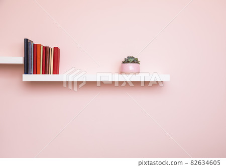 White bookshelf with books and potted plant on a pale pink wall 82634605