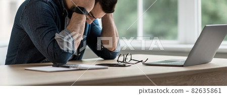 Tired unhappy young businessman holding head in hands upset about business failure Tired unhappy young businessman holding head in hands upset about business failure 82635861