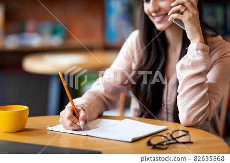 Looking for jop opportunity. Young woman talking on smartphone and taking notes, sitting at cafe interior Looking for jop opportunity. Young woman talking on smartphone and taking notes, sitting at cafe interior 82635868