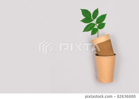 Eco-friendly coffee to go cups - mockup kraft paper cup with green leaves above on light gray background with copy space. Recycled kraft paper packaging and zero waste concept 82636880