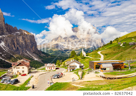 View to Passo Selva di Val Gardena whith Cappella di San Maurizio white chapel, Hotel and parking car with mountains Langkofel in the background. Dolomiti, Trentino Alto Adige, Dolomites alps, Italy 82637042