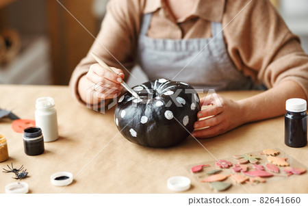Cropped shot of woman in apron painting Halloween pumpkin with paint brush in hand Cropped shot of woman in apron painting Halloween pumpkin with paint brush in hand 82641660