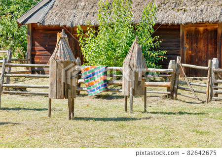 Vintage wooden beehives with a thatched roof against the backdrop of a rural courtyard brightly lit by the sun's rays. 82642675