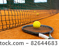 Close up tennis ball, racket and net on court. Close up of tennis ball on clay court. Red clay court. 82644683