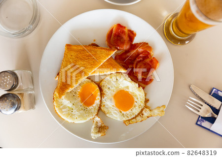 Fried eggs, roasted bacon slices and wheat bread toasts Fried eggs, roasted bacon slices and wheat bread toasts 82648319
