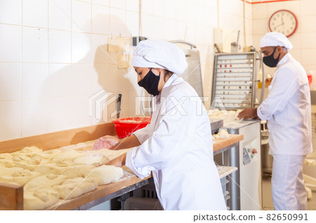 Bakery worker cuts raw dough with knife Bakery worker cuts raw dough with knife 82650991