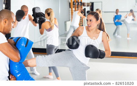 Woman kicking boxing shield in coach hands Woman kicking boxing shield in coach hands 82651020