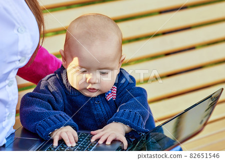 Woman sits on park bench with baby during online learning. Woman sits on park bench with baby during online learning. 82651546