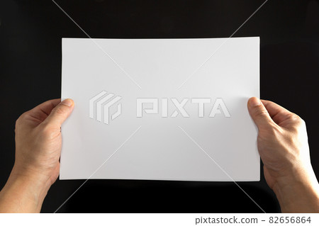 The concept of both hands that holds a white sheet of paper on a black background. 82656864