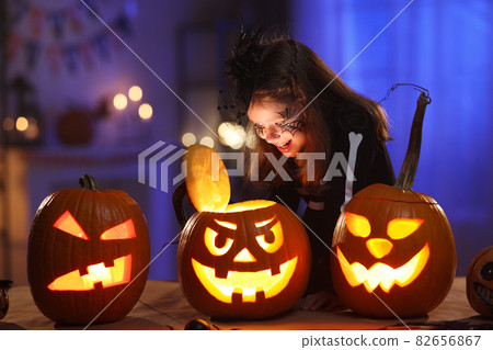 Little girl in Halloween costume and makeup with glowing jack-o-lantern during Halloween celebration Little girl in Halloween costume and makeup with glowing jack-o-lantern during Halloween celebration 82656867