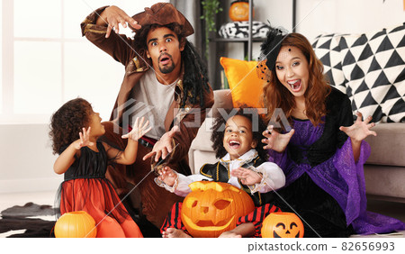 African american family in Halloween costumes making scary gesture while sitting with jack o lantern African american family in Halloween costumes making scary gesture while sitting with jack o lantern 82656993
