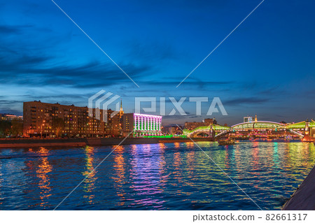 View of the colorful Bogdan Khmelnitsky bridge illuminated at night reflecting in the Moskova river. Moscow Kiyevsky railway station at night. Moscow, Russia 82661317