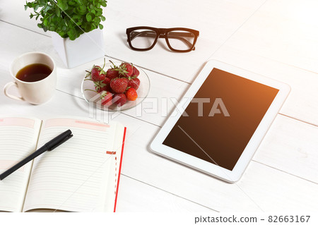 Office table desk with set of supplies, white blank notepad, cup, pen, tablet, glasses, flower on white background. Top view Office table desk with set of supplies, white blank notepad, cup, pen, tablet, glasses, flower on white background. Top view 82663167