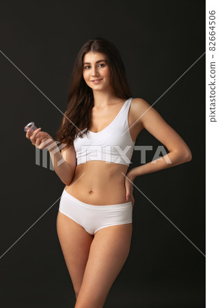 Portrait of young beautiful slim woman in white sportive lingerie posing isolated over dark studio background. Natural beauty concept. 82664506