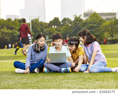 group of asian elementary school children sitting on playground grass looking at laptop computer group of asian elementary school children sitting on playground grass looking at laptop computer 82668275