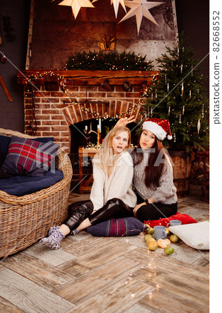 cheerful girlfriends in the New Year's decorations in the fireplace cheerful girlfriends in the New Year's decorations in the fireplace 82668552