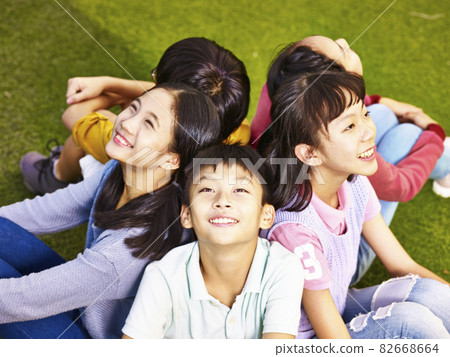 group of asian elementary school boys and girls sitting on playground grass looking up at the sky 82668664