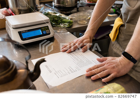 The baker looks through the recipe in the bakery on the table, dressed in an apron. 82669747