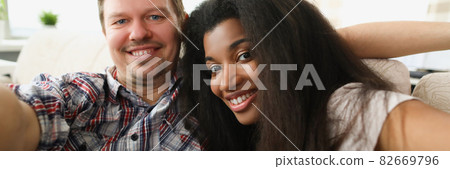 Cheerful multiethnic couple in love sits in embrace in cozy living room at home 82669796