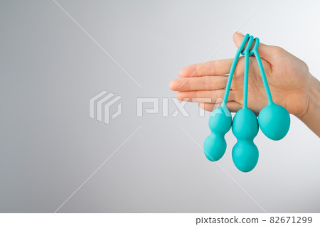 A faceless woman demonstrates a set of mint-colored vaginal balls. Girl holding a kegel trainer for training pelvic floor muscles on a white background. 82671299