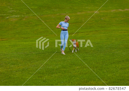 girl runs with a dog in the park on the lawn at sunset, walks a pet in nature. 82678547