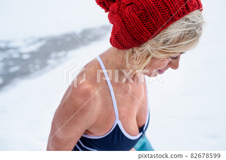 High angle view close up of active senior woman in wet swimsuit looking down outdoors in winter, cold therapy concept. High angle view close up of active senior woman in wet swimsuit looking down outdoors in winter, cold therapy concept. 82678599