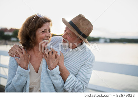 Happy senior couple in love hugging outdoors on pier by sea, looking at each other. 82679028