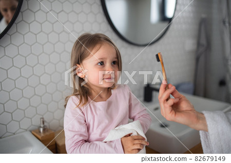 Unrecognizable mother with small daughter brushing teeth indoors in bathroom in the evening or morning. 82679149