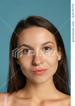 Close-up portrait of young beautiful girl without makeup isolated over blue studio background. Natural beauty concept. 82679743