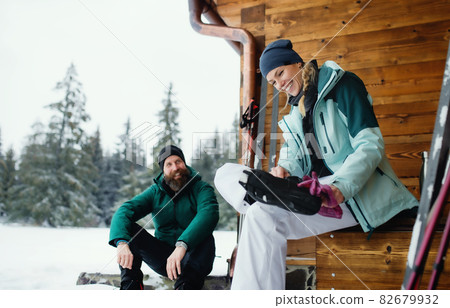 Mature couple resting by wooden hut outdoors in winter nature, cross country skiing. Mature couple resting by wooden hut outdoors in winter nature, cross country skiing. 82679932