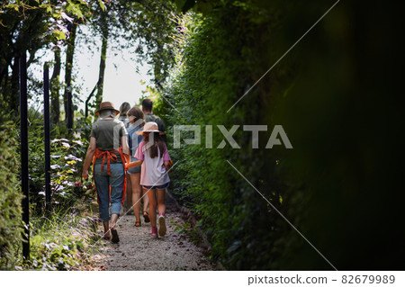 Rear view of happy young and old farmers or gardeners carrying their harvest outdoors at community farm. Rear view of happy young and old farmers or gardeners carrying their harvest outdoors at community farm. 82679989