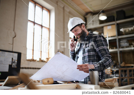 Low angle view of mature male carpenter looking at blueprints plans in carpentery workshop. Small business concept. 82680041