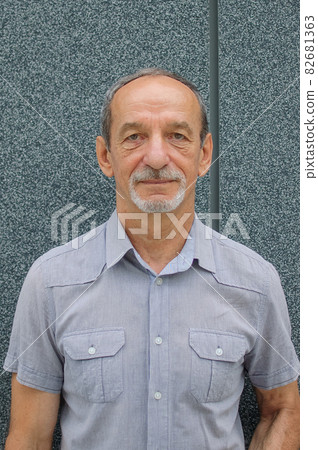 Male portrait of older coworker in blue shirt near dark grey wall Male portrait of older coworker in blue shirt near dark grey wall 82681363