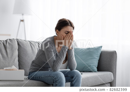 Sad caucasian millennial female covered face with hands, sitting on sofa and suffering from problems 82682399