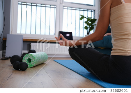Woman sitting in lotus position on blue mat at home 82682601